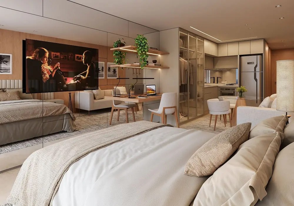 Studio com cama de casal, TV, bancada de trabalho e cozinha ao fundo